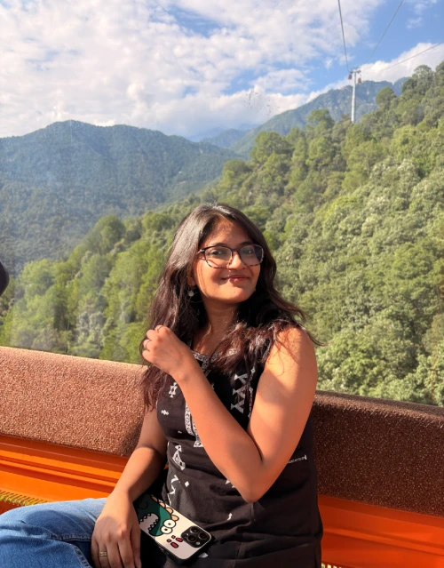Riya, a graphic designer, smiling while sitting inside a scenic mountain cable car surrounded by lush green hills.
