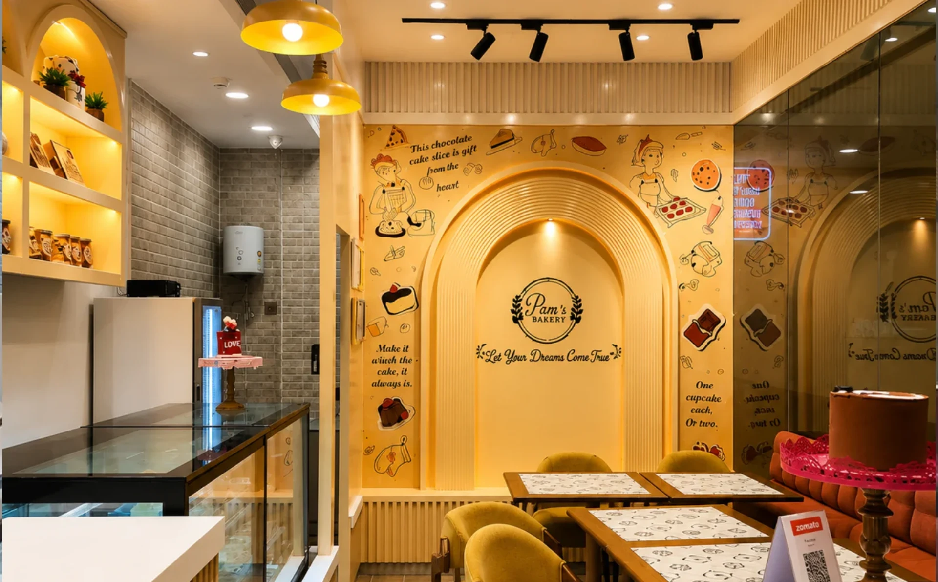 Pam Bakers bakery interior featuring a warm yellow-themed seating area, branded wall mural, display counters, and cake presentation.